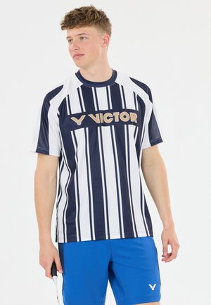 Ung mand iført en navy og hvidstribet Victor sportstrøje og blå shorts, der holder en badmintonketcher og kigger til siden.