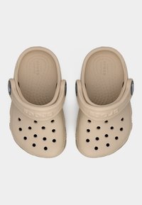 Ζευγάρι μπεζ Crocs από πάνω, με τρύπες αερισμού και ρυθμιζόμενα λουράκια στην φτέρνα με μαύρα κυκλικά λογότυπα.