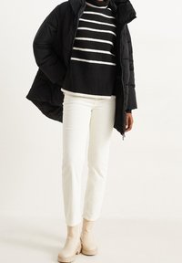 Czarna ocieplana kurtka, paskowany czarno-biały sweter, kremowe spodnie w korduroy oraz beżowe botki za kostkę. Skupienie na ciepłych teksturach i kontrastujących kolorach.