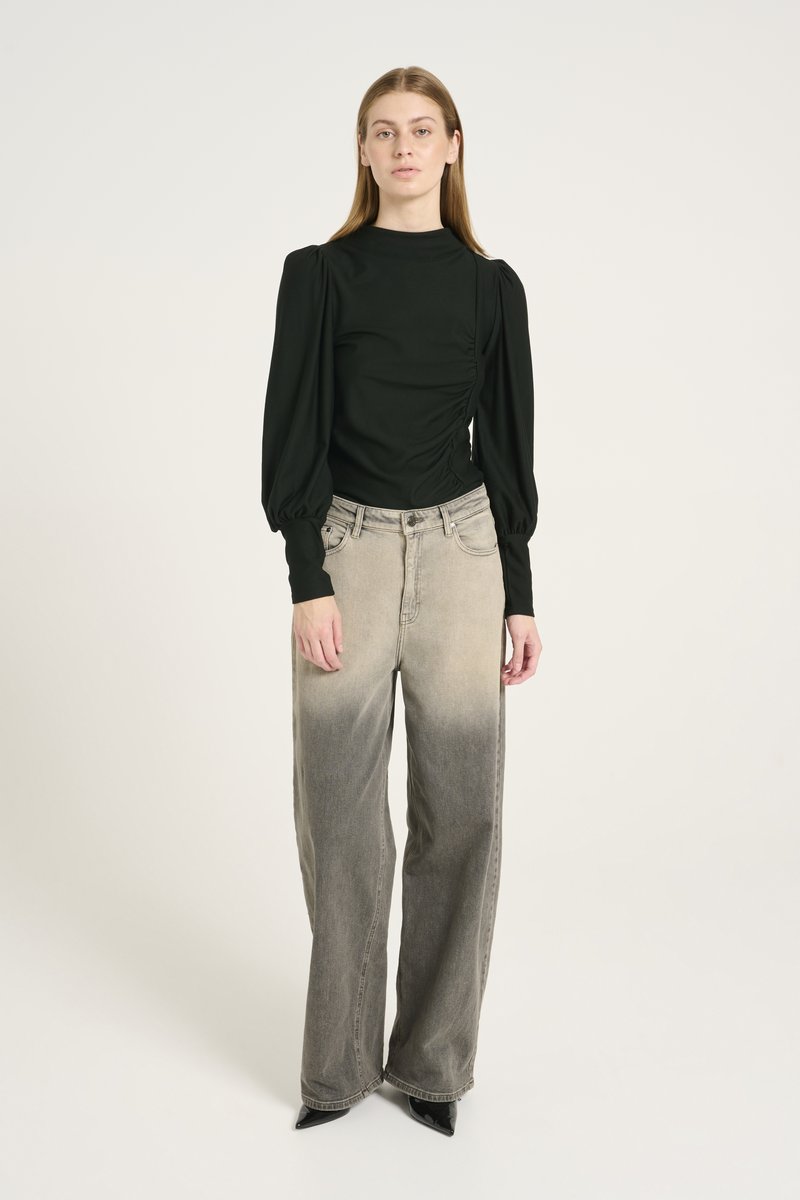 Black long-sleeve top with gathered side detail, paired with light grey, wide-leg jeans featuring an ombre effect. Black pointed-toe heels.