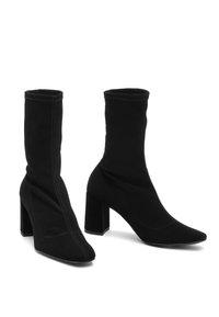 Bottes en cuir noires à la cheville, en tissu doux, avec un bout pointu, un talon bloc haut et un design de tige sans couture et ajusté. Détails de couture contrastants.