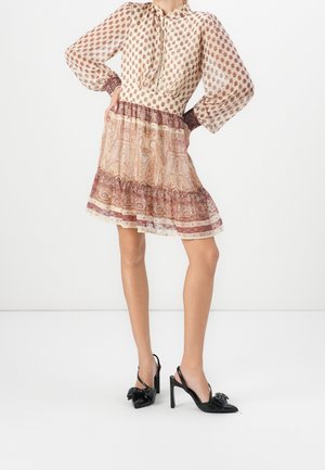 Femme portant une robe à manches longues à motif avec une jupe évasée et des escarpins slingbacks noirs à talons hauts, debout les mains sur les hanches.