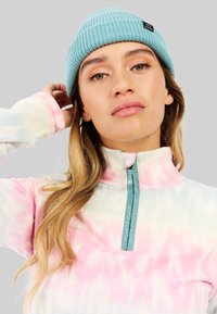 Fleece pullover in pastel tie-dye kleuren, met een hoge kraag en een halve rits in teal, gecombineerd met een lichte blauwe gebreide beanie.
