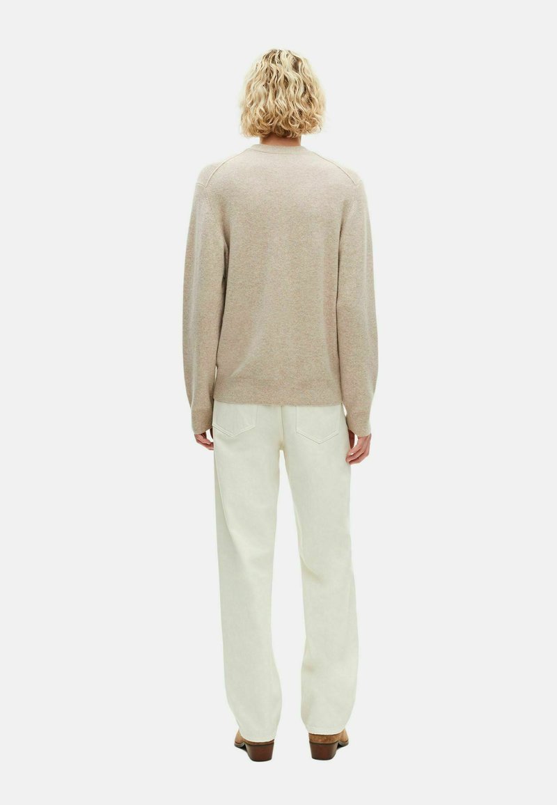 Beige gebreide trui met lange mouwen, ontspannen pasvorm en geribbelde zoom, gecombineerd met witte wijde broek en bruine hakken.