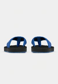 Ζευγάρι μπλε και μαύρες παντόφλες με ανάγλυφες σόλες, εμφανιζόμενες από μπροστά πάνω σε απλό λευκό φόντο.