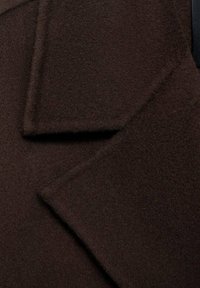 Tissu de manteau en laine brun avec une texture douce, présentant des revers aux bords nets et un design structuré. Pas de matériel ou d'accents visibles.