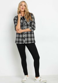 Camisa de franela a cuadros en blanco y negro con mangas remangadas, combinada con leggings negros y zapatillas blancas con detalles en beige. Diseño sencillo.