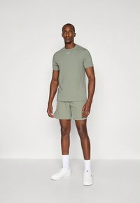 Conjunto atlético verde-claro composto por uma camisola de manga curta e calções, feito de material liso, combinado com ténis brancos e meias até ao tornozelo.