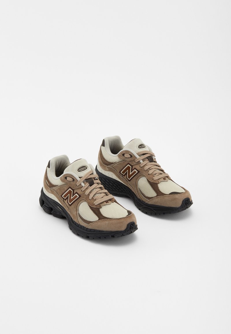 Baskets en mesh beige et marron avec empiècements en daim et semelles en caoutchouc noir, arborant un logo "N" bien visible, des lacets ronds et un col rembourré.