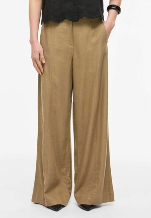 Pantaloni bej cu croială largă purtați cu un top negru cu margine ondulată, o brățară neagră și pantofi negri cu vârf ascuțit.