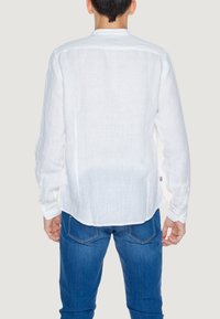 Camicia bianca in lino a maniche lunghe con polsini abbottonati, orlo curvo e una texture liscia, abbinata a jeans in denim blu.