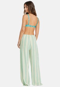 Bralette floral turquoise avec des bretelles ajustables associé à un pantalon léger crème avec des rayures verticales vertes et une coupe décontractée.