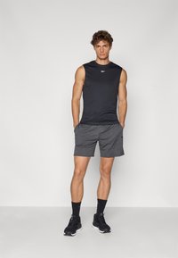 Camisola atlética preta sem mangas, calções cinzentos com bolsos, tecido texturizado, combinada com sapatilhas pretas e meias pretas, de pé sobre um fundo neutro.