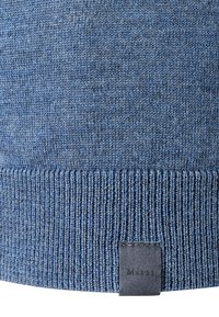 Modrá pletená svetr s ribovaným lemem, měkkou texturou a malou černou nášivkou s nápisem "März" na spodní straně.