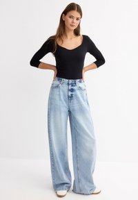 Bodysuit negro de manga larga combinado con jeans de tiro alto de pierna ancha en un suave tono azul claro. Textura de denim suave con sutiles detalles de desgaste y diseño clásico de cinco bolsillos.