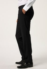 Pantaloni neri con taglio dritto, dotati di tasche laterali e una texture liscia. Indossati con scarpe eleganti nere lucide.