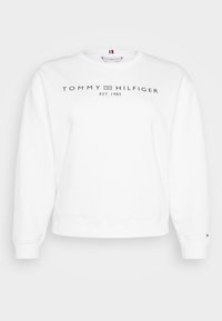Sudadera blanca, de cuello redondo, fabricada con una mezcla de algodón, presenta "TOMMY HILFIGER EST. 1985" en texto negro, puños y dobladillo acanalados, pequeño logo en la manga.