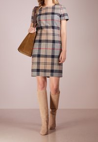Geruite jurk in beige, grijs en marineblauw met korte mouwen, gecombineerd met tan suède laarzen tot de knie en een bijpassende bruine handtas.