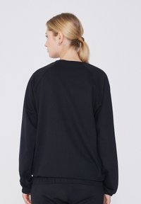 Sudadera negra de manga larga, diseño raglán, cintura elástica y textura suave. Costuras claramente visibles y superficie trasera lisa.