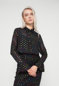 Μαύρο πουκάμισο με κουμπιά, διακοσμημένο με πολυχρωμαίες βούλες, διαθέτοντας γιακά, μακριά μανίκια και φαρδιές μανσέτες. Λείο και ελαφρύ ύφασμα.