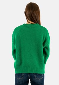 Suéter verde de punto con un corte holgado, cuello redondo y dobladillo acanalado. Textura suave con un patrón sutil y hombros caídos.