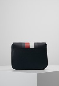 Bolso sintético negro con rayas horizontales en rojo, blanco y azul en la parte superior. Presenta una forma rectangular elegante y un cierre de cremallera.