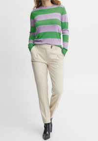 Maglione a righe verde e lavanda, con maniche lunghe, abbinato a pantaloni beige su misura con dettagli a doppio bottone e pieghe.