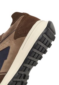 Sneaker in suede marrone con un pannello blu scuro a contrasto, suola in gomma testurizzata con scanalature profonde e dettagli di cucitura discreti.