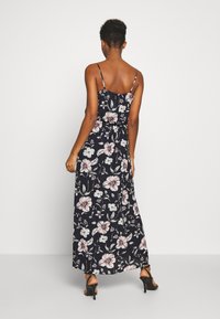 Robe maxi florale avec un fond marine, ornée de fleurs roses et blanches, à fines bretelles spaghetti, et un corsage ajusté s'évasant en une jupe large.