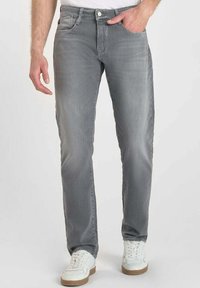 Vaqueros de mezclilla gris con corte recto, bolsillos frontales y cierre de botón. Llevados con zapatillas blancas, que presentan una textura suave.