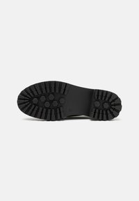 Black rubber boot sole with hexagonal treads, featuring a flat surface and ridged edges for traction. Simple and functional design.