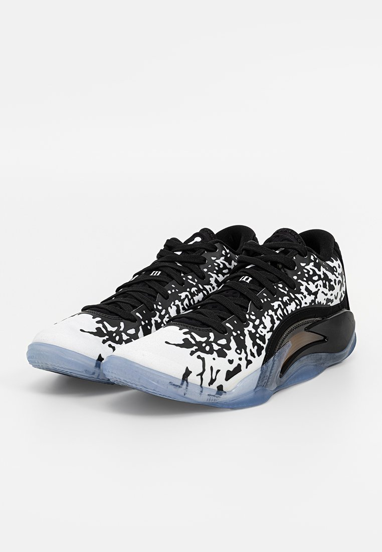 Des chaussures de sport avec un design éclaboussé en noir et blanc, comportant un matériau supérieur lisse et une semelle en caoutchouc translucide. Accents noirs sur le côté.