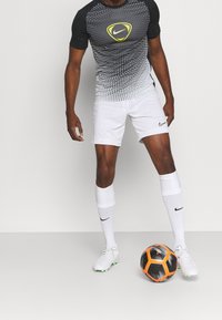 Odzież sportowa Nike z czarno-białą koszulką z krótkim rękawem w gradient, z logo, w połączeniu z białymi szortami i piłkarskimi skarpetami, trzymając piłkę.