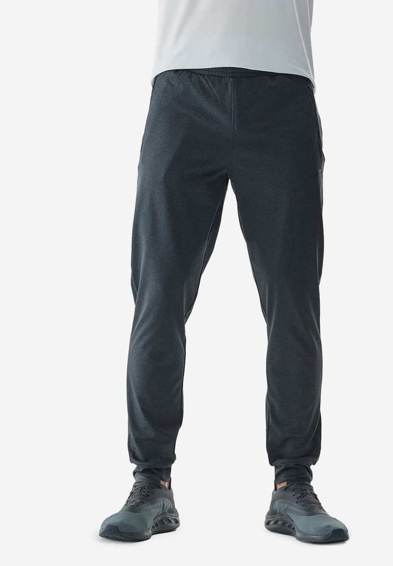 Pantalones deportivos de color gris oscuro con una textura suave, ajuste ceñido, cinturilla elástica y bolsillos laterales, combinados con zapatillas deportivas negras.
