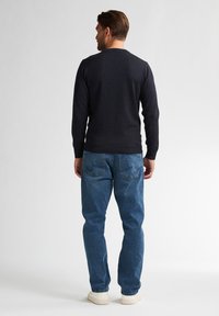 Granatowy sweter z długimi rękawami, okrągłym dekoltem. W połączeniu z jasnoniebieskimi dżinsami, widocznymi szwami i tylnymi kieszeniami. Na nogach białe trampki.