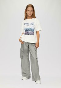 Weißes Grafik-T-Shirt mit einem Stadtbilddruck und dem Text "Dreaming" in Pink, kombiniert mit grauen Cargo-Hosen und weißen Sneakern.
