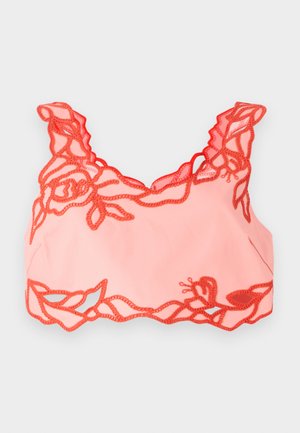 Ljusrosa bralette med röd blommig spetskant längs kanterna och scallopade axelremmar, tillverkad av mjukt tyg för en slät finish.