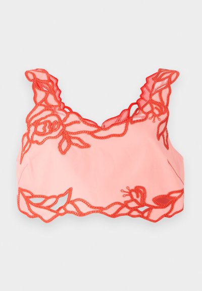 Helles rosa Bralette mit rotem, blütenförmigem Spitzenbesatz entlang der Kanten und gewellten Trägern, gefertigt aus weichem Material für eine glatte Oberfläche.