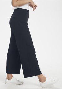Wide-leg trousers in dark blue fabric with a smooth texture, featuring a high waistband and a back pocket. Pairing with white sneakers.