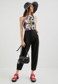 Top halter impreso y colorido con patrones geométricos; pantalones de tiro alto negros; sandalias rosas; bolsa negra con correa; sombrero de ala ancha.