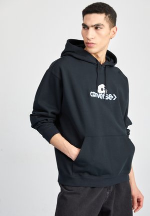 Sudadera negra de mezcla de algodón, con un bolsillo canguro y un logo blanco con diseño de calavera en el pecho. Corte holgado, textura suave.