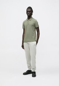 Olivově zelené polo tričko s límečkem, v kombinaci s světle šedými tepláky s předním logem a černými sportovními botami.