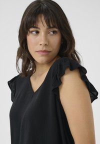 Blouse noire avec des manches courtes à volants, design en V, fabriquée en tissu léger texturé. Surface lisse avec un léger éclat.