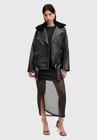 Μαύρο δερμάτινο μπουφάν με κολάρο από ψεύτικη γ�ούνα, επενδυμένο πάνω από ένα εφαρμοστό μαύρο φόρεμα με διαφανή και συμπαγή πάνελ, που διαθέτει πλευρική σχισμή. Ασημένια τακούνια.