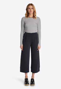 Zwarte wijde broek met een gladde stof, hoge tailleband en omgeslagen zoom, gecombineerd met een getailleerd zwart-wit gestreept shirt met lange mouwen.