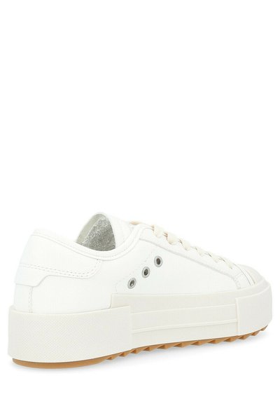 Sneaker bianco in tela con suola in gomma spessa, punta rotonda e cinque occhielli per i lacci. Presenta un interno testurizzato e una suola in gomma marrone.