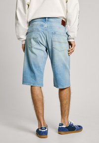 Shorts de mezclilla azul claro con un ajuste relajado, con bolsillos traseros tipo parche y sutiles detalles de costura. Llevados con zapatillas azul.