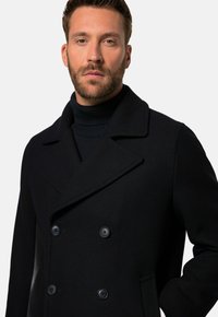 Abrigo negro tipo peacoat con un diseño de doble botonadura, grandes solapas rectas, dos botones y bolsillos laterales. Textura de lana suave.