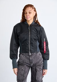 Zwarte bomberjack met een aansluitende taille, ribgebreide manchetten en een zilveren rits. Bevat een patchzak met een rode label op de mouw.
