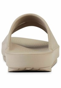 Beige slide sandal with a wide, open back, smooth matte texture, and a thick sole featuring a subtle wave pattern for grip.